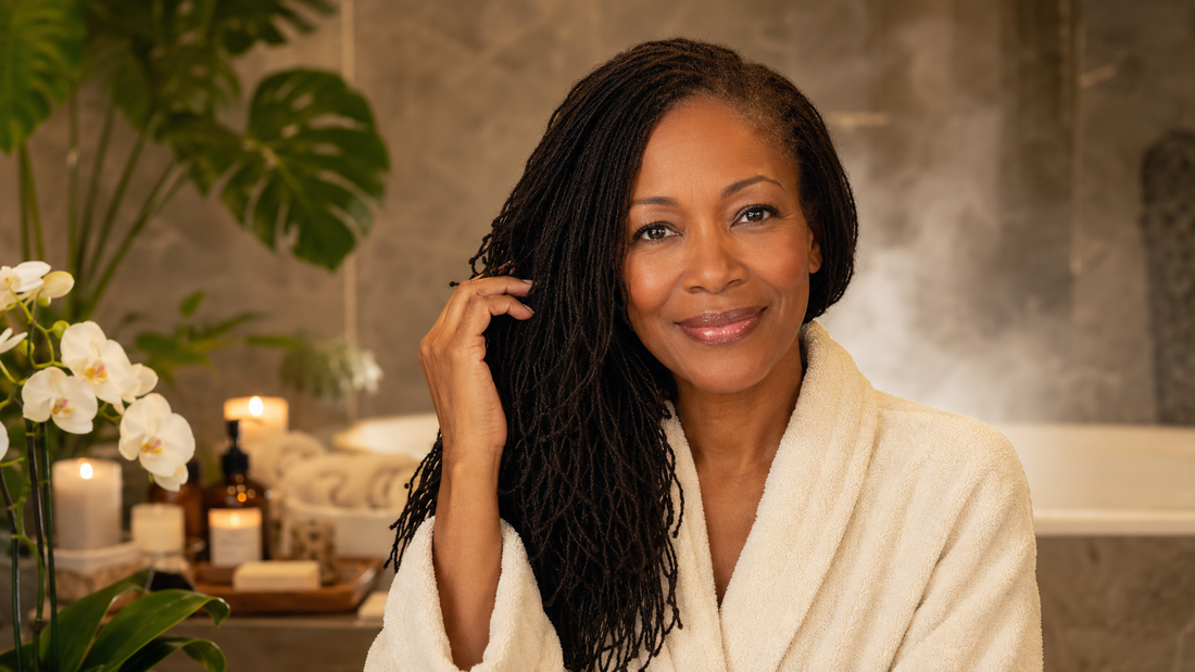 Mid-aged Black woman with long healthy Sisterlocks touching her hair in a peaceful spa setting, representing hydrated Sisterlocks and hair porosity care.
